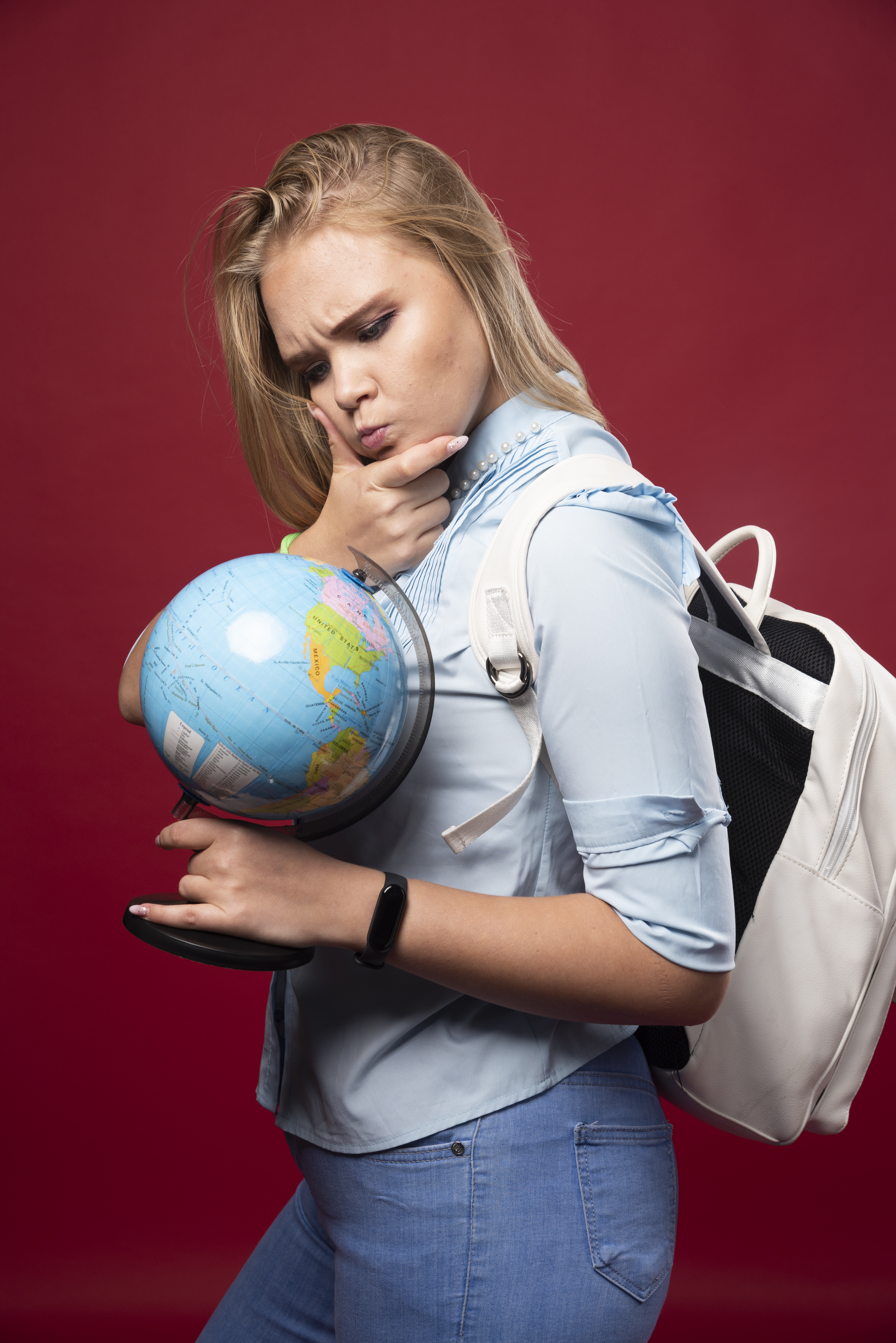 Blonde studentgirl holds a globe and looks surprized. High quality photo